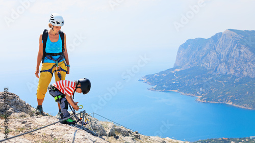 Fotografi Young mother, child in safety equipment climb to mount top by via ferrata beginner route