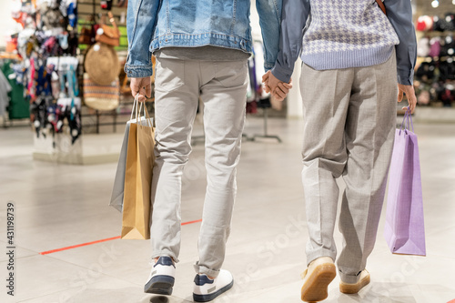 A pair of people in casualwear walking in the mall with shopping bags