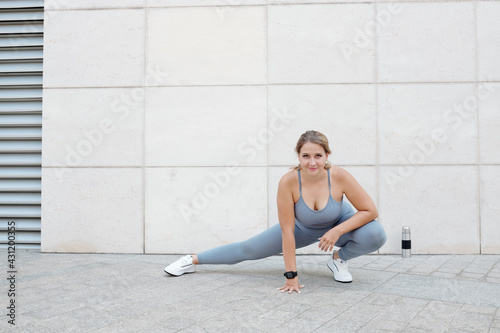Pretty smiling young plus size woman doing side lunges and bending forward to stretch legs and strengthen thighs