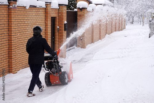 A man after a snowfall removes snow with a snowplow. Snow removal with a gasoline sweeper.