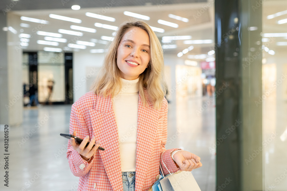 Happy young blond woman holding a phone and paperbags