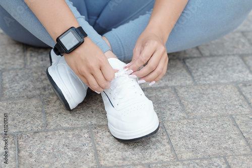 Close-up image of sportswoman with smartwatch on her wrist tying shoelaces and getting ready for training