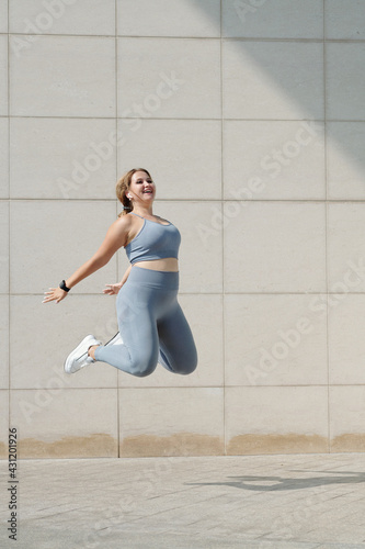 Happy excited young plus size woman jumping high, healthy lifestyle and workout concept