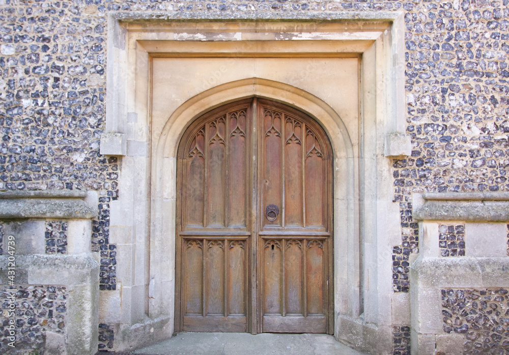 Old wooden door to Christian church embedded in flint stone wall