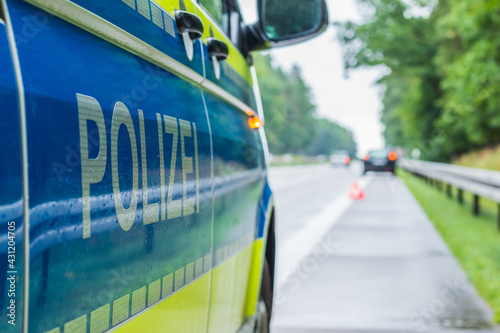 Police car on the highway in a side perspective during an accident. Lettering police on the body with boom and yellow background. Hard shoulder, lane and crash barriers with trees photo