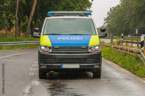 Police car on the highway. Front view of a vehicle from the state of Brandenburg in a parking lot. Asphalt roadway of an emergency stop. Trees and crash barriers with road signs in the background