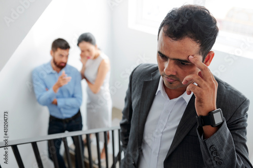 Businessman tired of hearing gossips behind his back, he is walking up the stairs and eavesdropping on conversation of colleagues photo