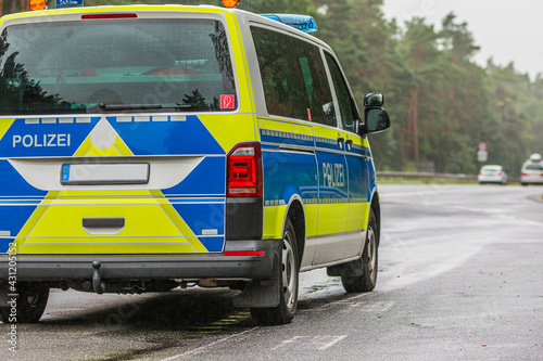 Police car on the Autobahn in the state of Brandenburg. Asphalted road surface in rainy weather. Angled view of the vehicle from behind. yellow and blue paintwork. Trees and guard rails