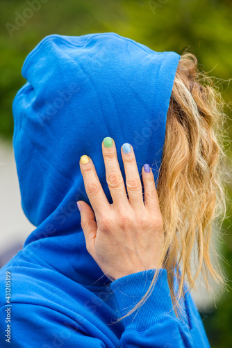 Young blonde woman wearing a blue hoodie, hand with rainbow-colors nail polish