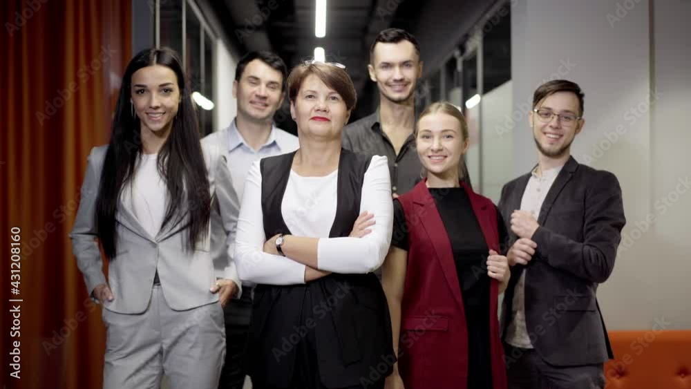 Group of Caucasian coworkers posing in office corridor. Confident successful men and women looking at camera smiling standing at workplace. Teamwork and team spirit concept Group of Caucasian coworkers posing in office corridor. Confident successful men and women looking at camera smiling standing at workplace. Teamwork and team spirit concept