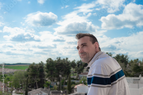 An attractive adult Caucasian man looking at the horizon from a balcony with the sky out of focus in the background.