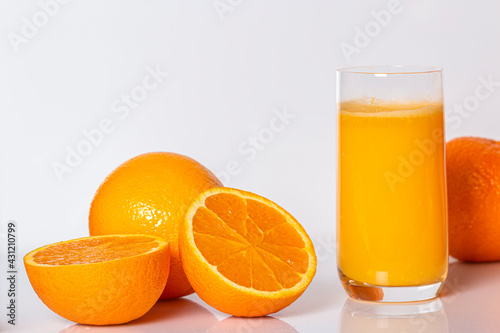 oranges lie on a white background next to a filled orange juice glass, photo