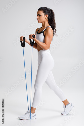 Fitness woman working out with resistance band on gray background. Athletic girl exercises with expander photo