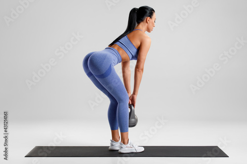 Fitness woman doing deadlift exercise for glutes on gray background. Athletic girl working out with kettlebell