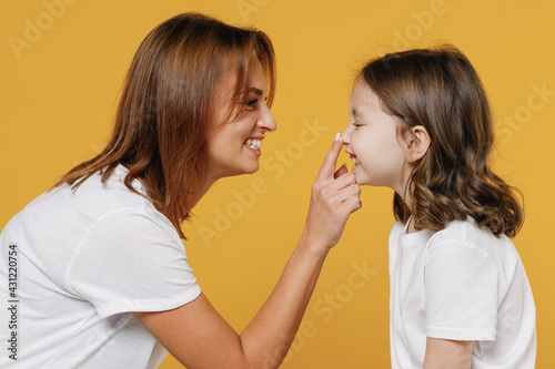 Happy woman in basic white t-shirt have fun with cute child baby girl 5-6 years old touch nose. Mommy little kid daughter isolated on yellow color background studio. Mother's Day love family concept.