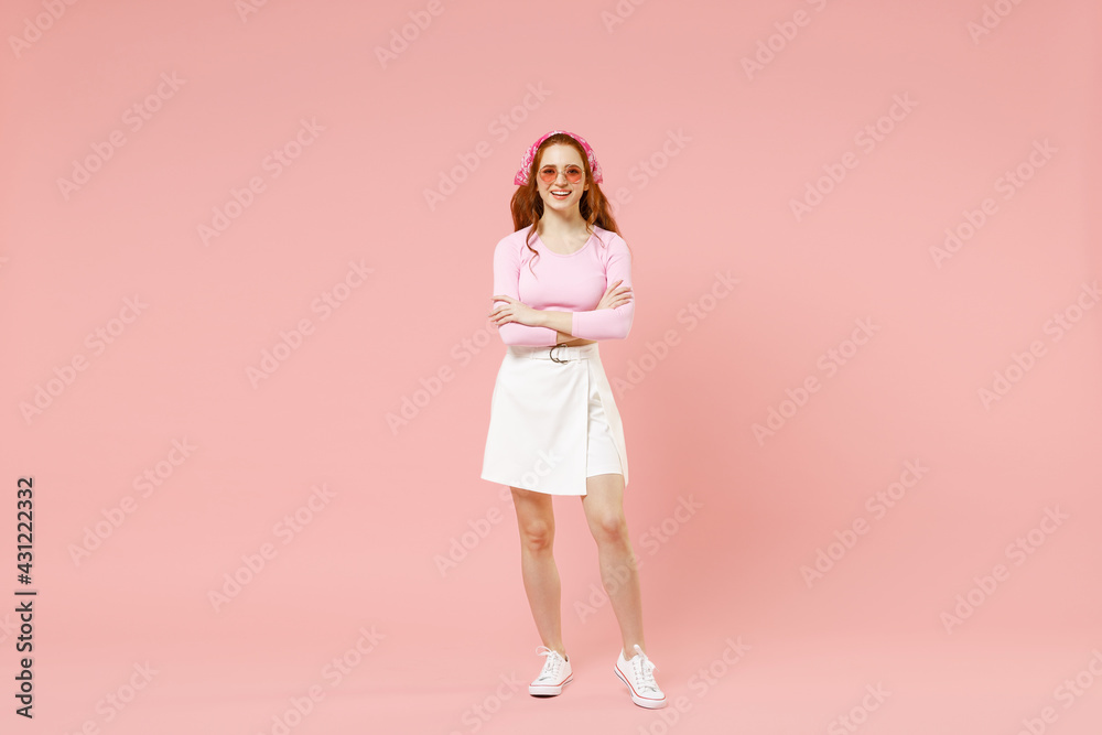 Full length young fun smiling happy trendy stylish caucasian woman in rose clothes bandana glasses hold hand cross folded isolated on pastel pink background studio portrait. People lifestyle concept