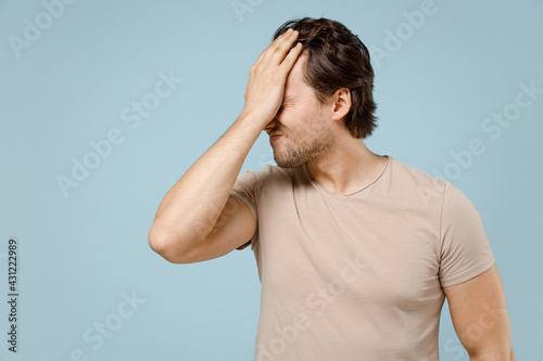 Young confused mistaken ashamed caucasian man 20s wearing casual basic beige t-shirt put hand on face facepalm epic fail gesture isolated on pastel blue background studio portrait. LIfestyle concept.