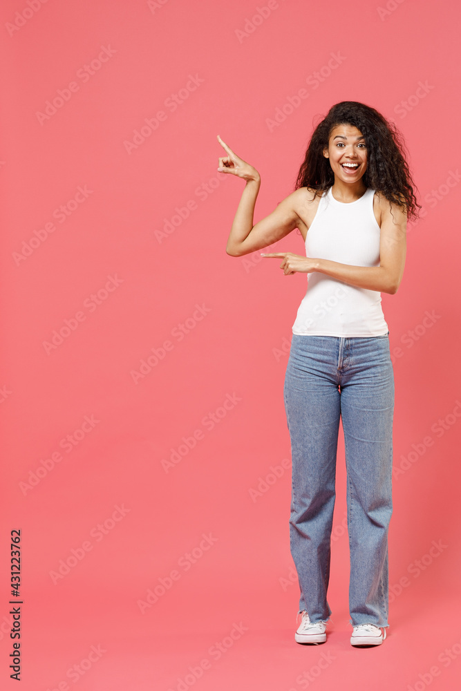 Full length young fun smiling happy positive african american woman 20s wear casual white tank shirt walk go point index finger aside on copy space area mock up workspace isolated on pink background Full length young fun smiling happy positive african american woman 20s wear casual white tank shirt walk go point index finger aside on copy space area mock up workspace isolated on pink background