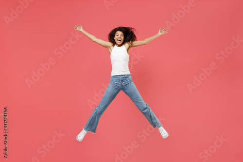 Full length young fun overjoyed happy joyful cheerful positive african american woman in casual white tank shirt jump high with outstretched hands isolated on pink color background studio portrait