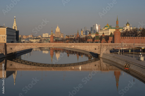 View of the Moscow Kremlin, river and stone bridge. Early morning. Reflection in smooth water. Skyscrapers and church in the background