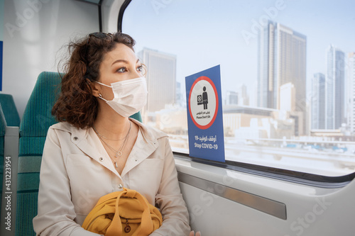 Photography Asian woman wearing a protective face mask sits on a subway seat and looks hopefully out the window with Dubai views