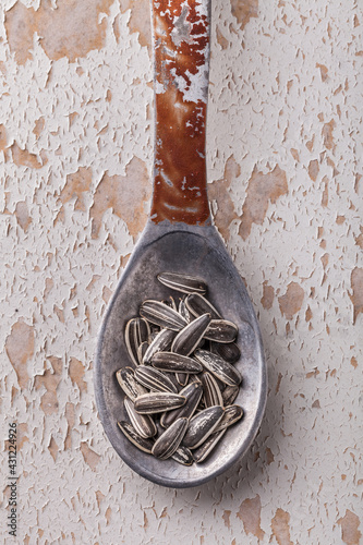 Sunflower seeds overhead large close-up arrangement in old metal spoon on old white rustic wooden table ready to eat studio shot