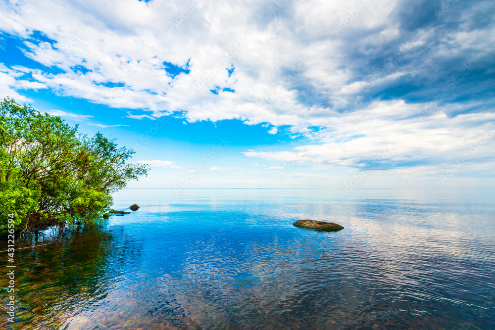 The boundless lake surface in calm weather. View from the shore. Stones in the water. Cumulus clouds. Summer day. Beautiful nature. Russia, Europe.
