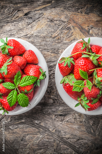 Strawberries fresh overhead ready to eat spring arrangement with green leaves in white ceramic jars on wooden table in studio
