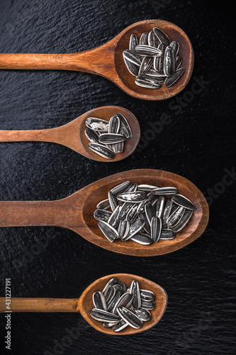 Sunflower seeds large overhead close-up arrangement in old wooden spoons on black shiny stone kitchen restaurant table studio shot
