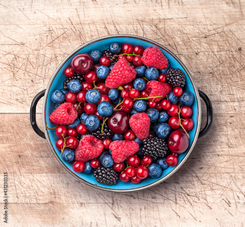 Berries mix fresh assortment ready to eat arrangement in rustic old blue metal plate on old kitchen wooden table overhead studio shot