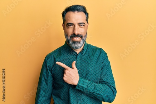 Middle age man with beard and grey hair wearing business clothes cheerful with a smile of face pointing with hand and finger up to the side with happy and natural expression on face