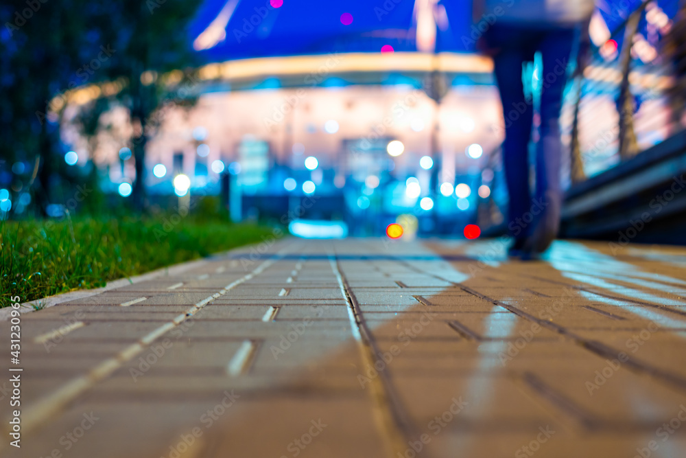 Illumination on the building. A man is walking along the road. Alley with trees and lanterns. Grass growing on the lawn. Close up view from the level of paved sidewalk. Illumination on the building. A man is walking along the road. Alley with trees and lanterns. Grass growing on the lawn. Close up view from the level of paved sidewalk.