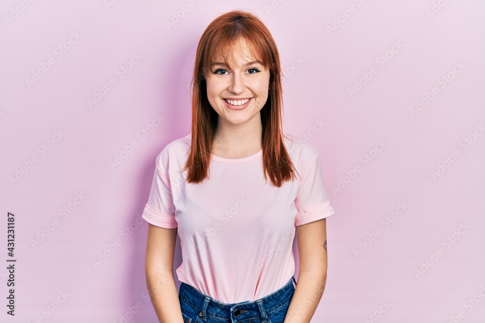 Redhead young woman wearing casual pink t shirt with a happy and cool smile on face. lucky person. Redhead young woman wearing casual pink t shirt with a happy and cool smile on face. lucky person.