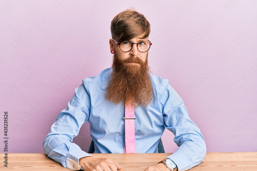 Young irish redhead man wearing business shirt and tie sitting on the table skeptic and nervous, frowning upset because of problem. negative person. Young irish redhead man wearing business shirt and tie sitting on the table skeptic and nervous, frowning upset because of problem. negative person.