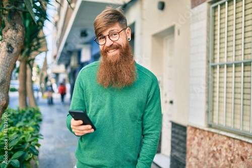 Young irish man with redhead beard smiling happy and using smartphone at the city.