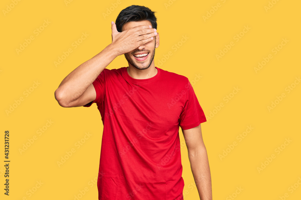 Young handsome man wearing casual red tshirt smiling and laughing with hand on face covering eyes for surprise. blind concept.
