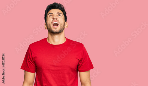 Young handsome man wearing casual red tshirt angry and mad screaming frustrated and furious, shouting with anger. rage and aggressive concept.