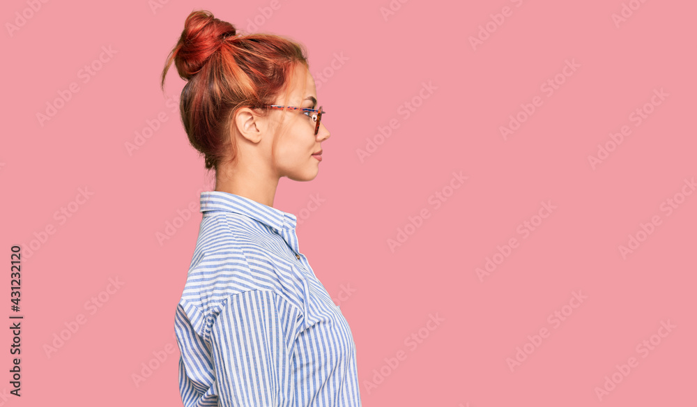 Young redhead woman wearing casual clothes and glasses looking to side, relax profile pose with natural face with confident smile. Young redhead woman wearing casual clothes and glasses looking to side, relax profile pose with natural face with confident smile.