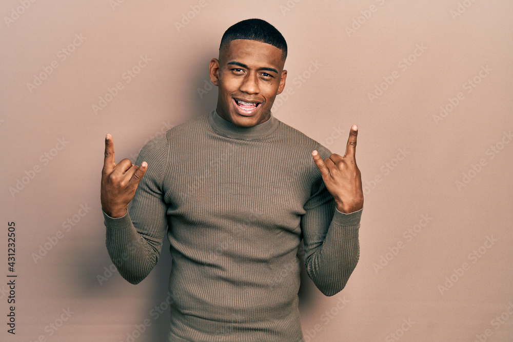 Fototapeta premium Young black man wearing casual turtleneck sweater shouting with crazy expression doing rock symbol with hands up. music star. heavy concept.