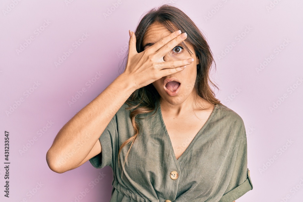 Young brunette woman wearing casual clothes peeking in shock covering face and eyes with hand, looking through fingers afraid Young brunette woman wearing casual clothes peeking in shock covering face and eyes with hand, looking through fingers afraid