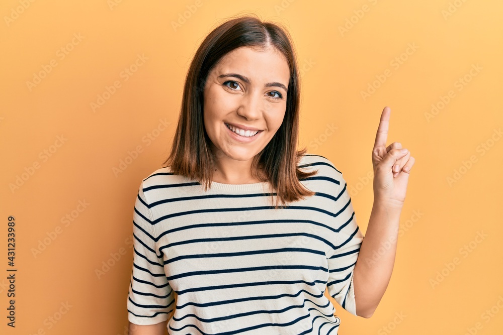 Young beautiful woman wearing casual striped t shirt smiling with an idea or question pointing finger up with happy face, number one Young beautiful woman wearing casual striped t shirt smiling with an idea or question pointing finger up with happy face, number one