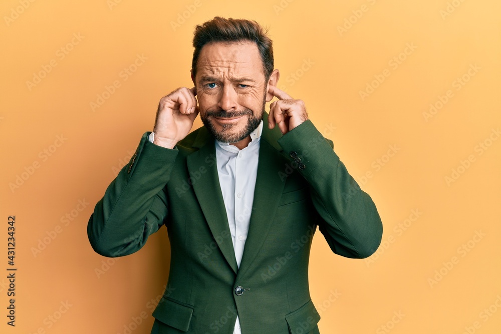Middle age man wearing business suit covering ears with fingers with annoyed expression for the noise of loud music. deaf concept. Middle age man wearing business suit covering ears with fingers with annoyed expression for the noise of loud music. deaf concept.