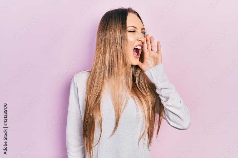 Young blonde girl wearing casual clothes shouting and screaming loud to side with hand on mouth. communication concept. Young blonde girl wearing casual clothes shouting and screaming loud to side with hand on mouth. communication concept.