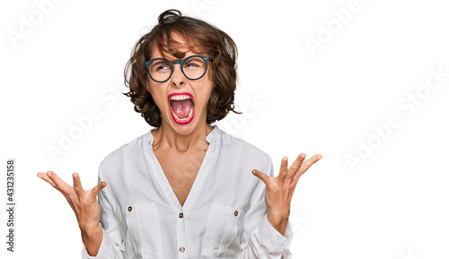 Young hispanic woman wearing business style and glasses crazy and mad shouting and yelling with aggressive expression and arms raised. frustration concept.