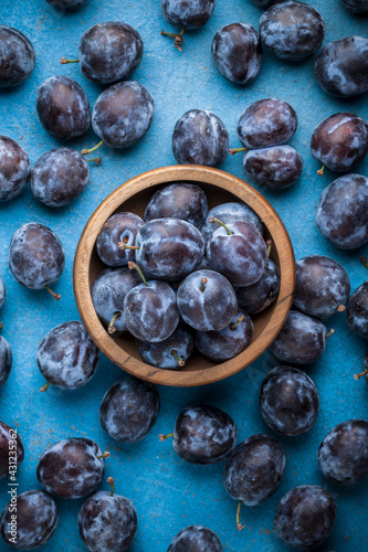 Fresh plums overhead ripe vibrant arrangement in old wooden jar on old blue kitchen table ready to eat studio shot
