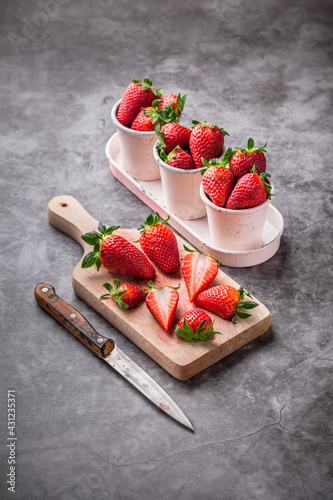 Strawberries fresh ready to eat arrangement in tin cans with kitchen knife wooden cutting board and gray marble background