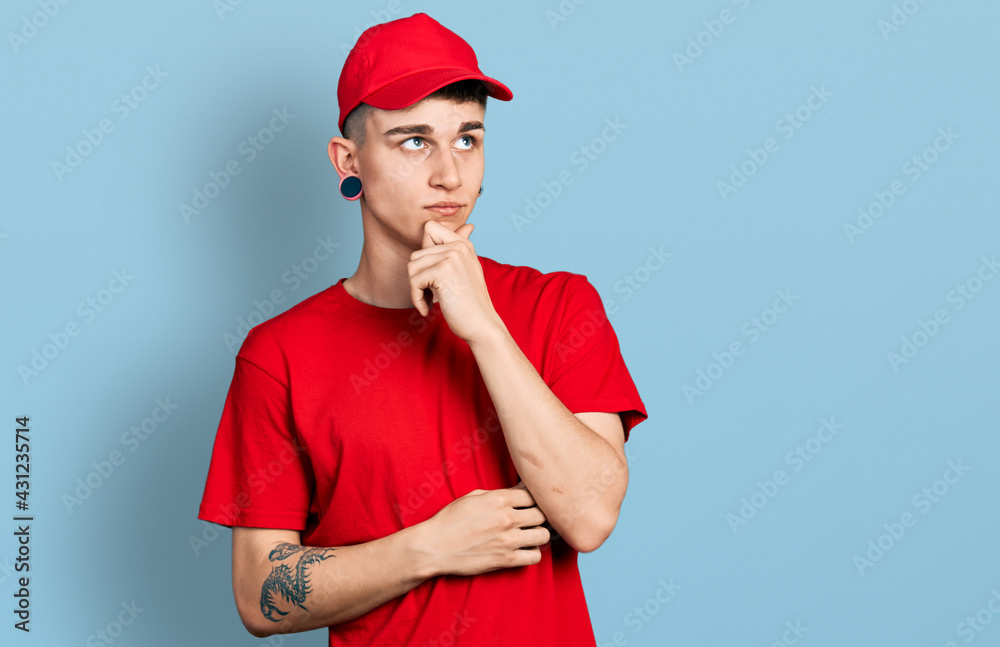Young caucasian boy with ears dilation wearing delivery uniform and cap serious face thinking about question with hand on chin, thoughtful about confusing idea Young caucasian boy with ears dilation wearing delivery uniform and cap serious face thinking about question with hand on chin, thoughtful about confusing idea
