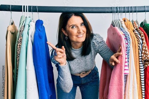 Middle age brunette woman working as professional personal shopper smiling happy pointing with hand and finger to the side