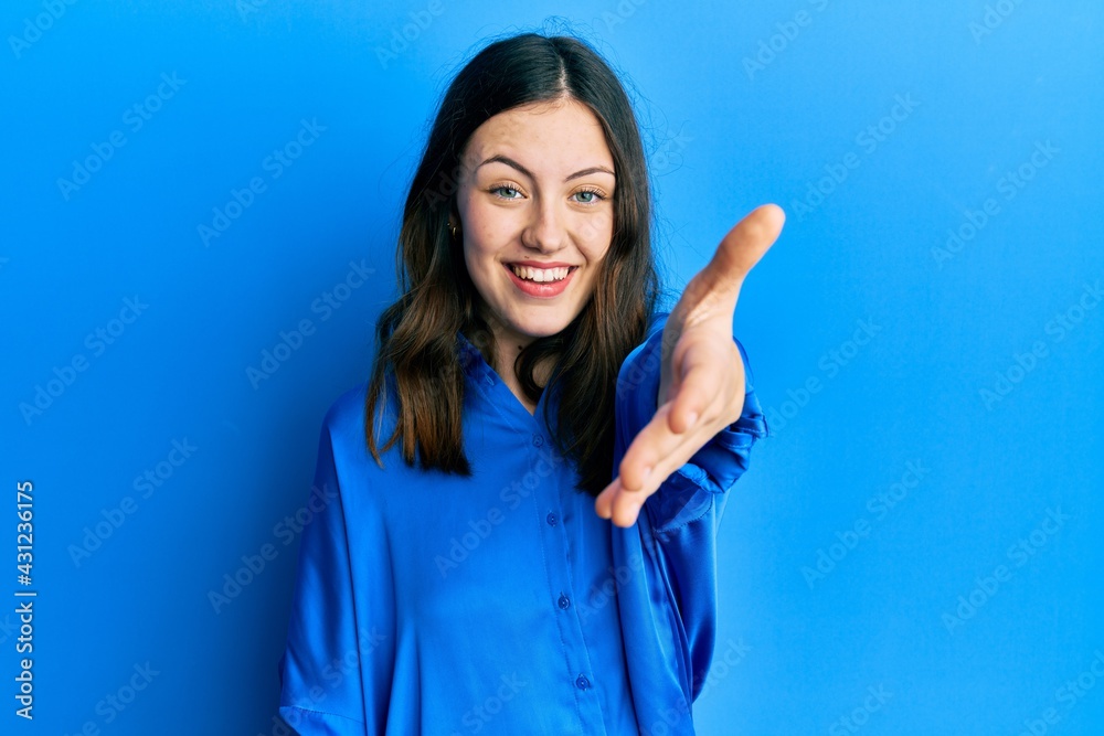 Young brunette woman wearing casual blue shirt smiling friendly offering handshake as greeting and welcoming. successful business. Young brunette woman wearing casual blue shirt smiling friendly offering handshake as greeting and welcoming. successful business.