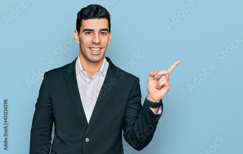Handsome hispanic man wearing business clothes with a big smile on face, pointing with hand finger to the side looking at the camera.